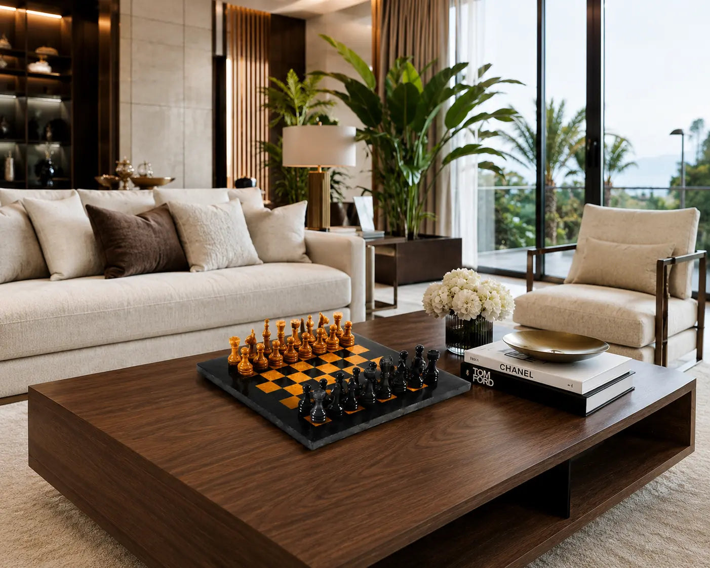A modern living room interior with a large dark wood coffee table in the foreground, holding a chess set and books. A cream sofa, matching armchair, plants, and floor-to-ceiling windows are visible in the room.