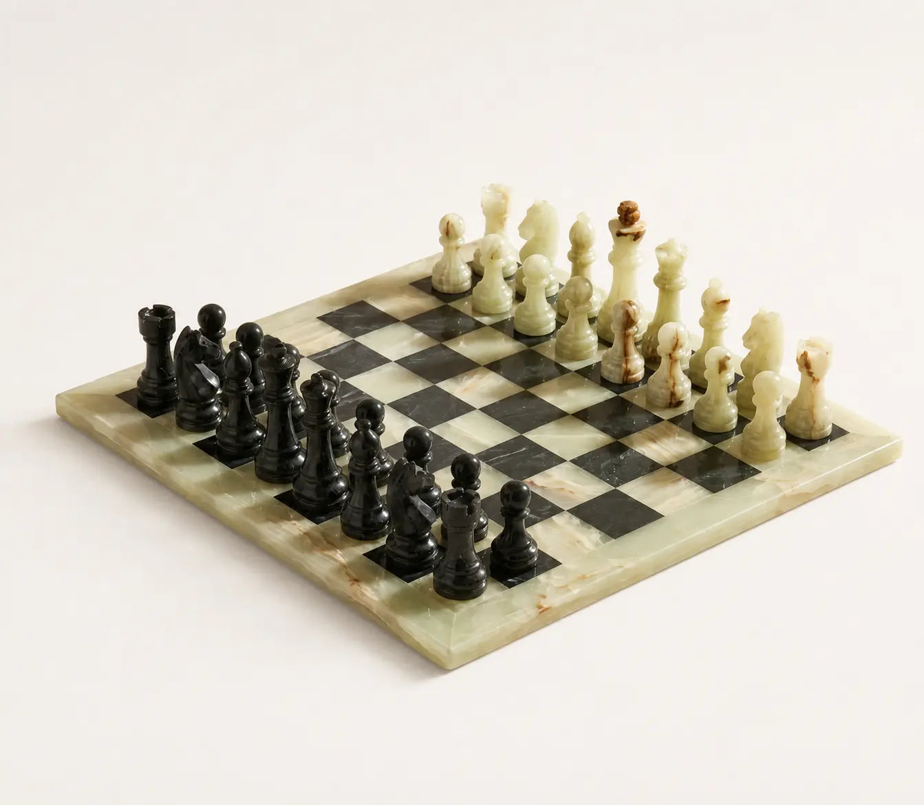 A polished stone chess set on a light cream background. The set includes a rectangular board with black and cream checkered squares, made from marbled stone, with black and cream chess pieces arranged in their starting positions.