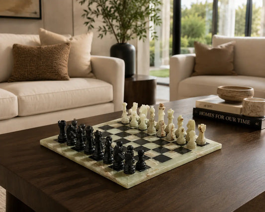 A marble chessboard with black and cream chess pieces displayed on a dark wood coffee table in a modern living room setting.