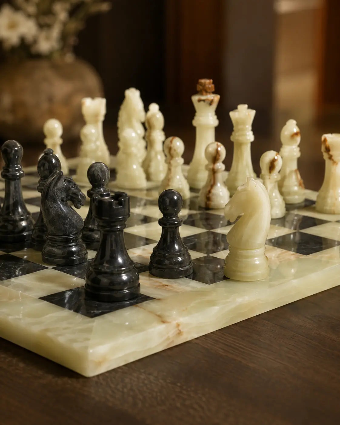 A polished marble chess set on a dark wooden table, featuring cream-colored and black-and-white marbled pieces and board squares.