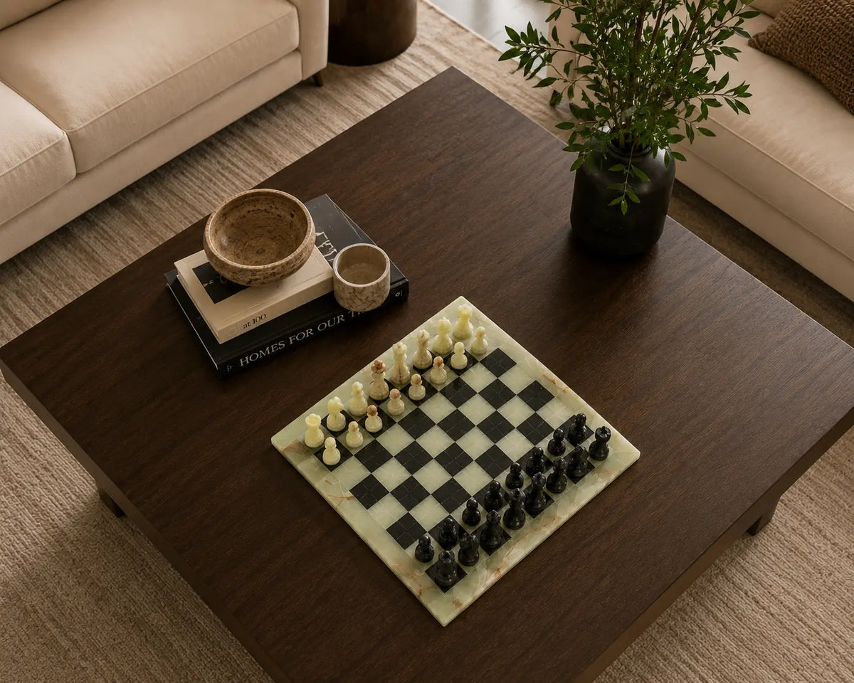 A marble chessboard with black and cream chess pieces on a dark wood coffee table in a modern living room setting.