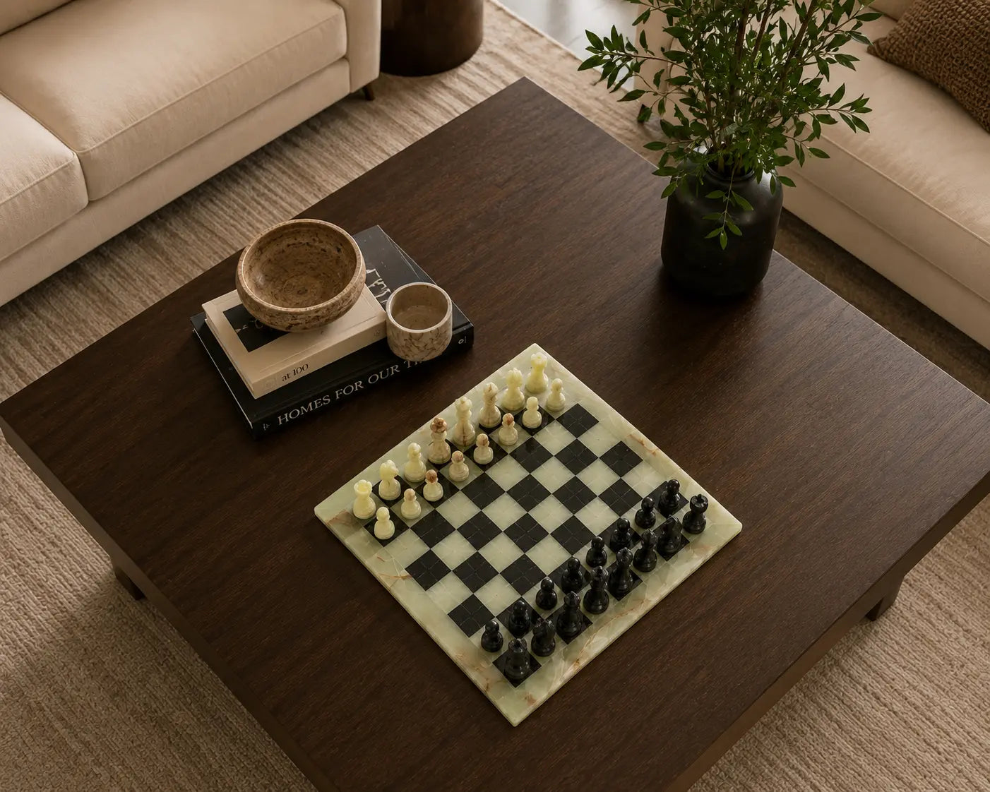 A marble chessboard with black and cream chess pieces on a dark wood coffee table in a modern living room setting.