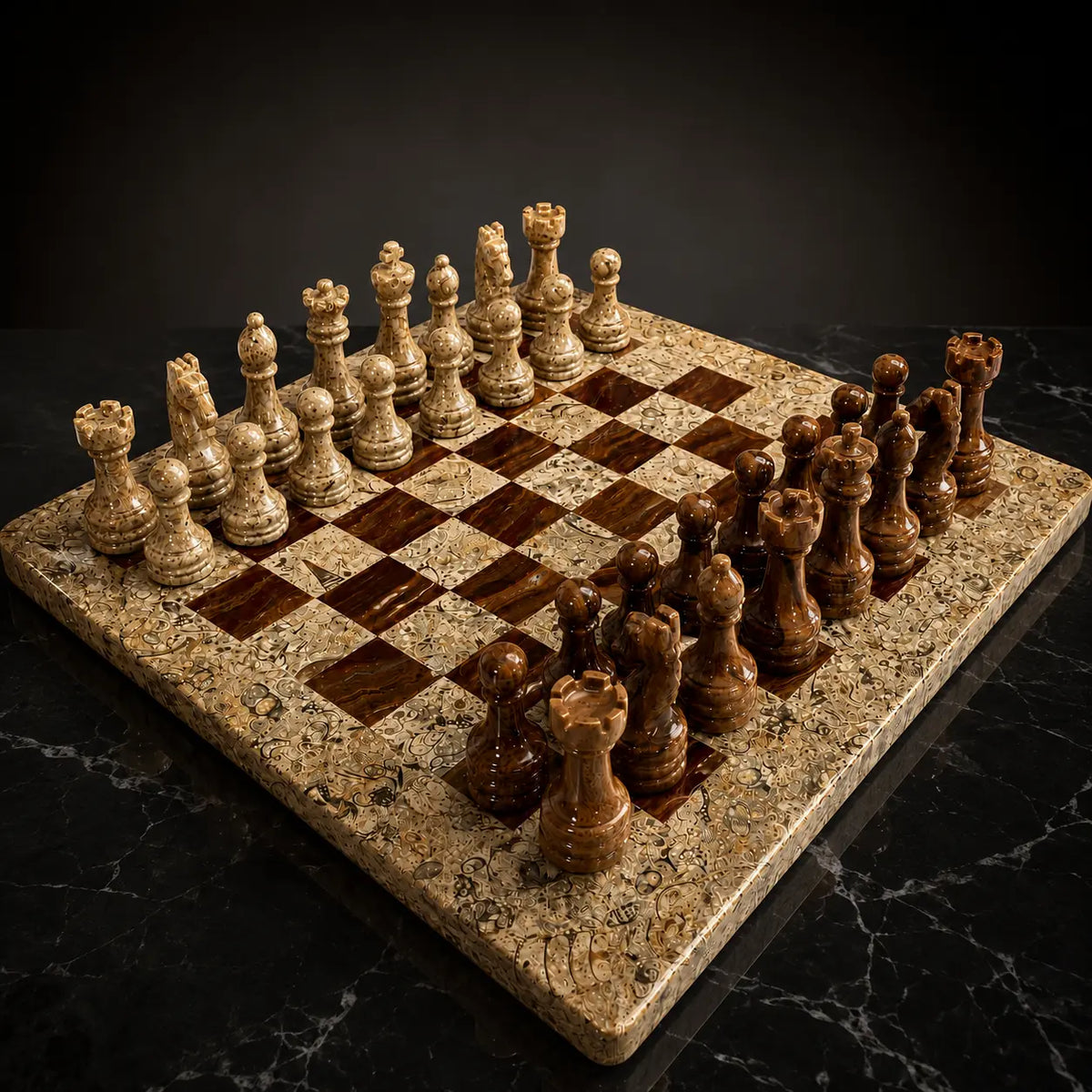 A polished stone chess set with cream and dark brown pieces arranged on a matching marble chessboard, photographed on a dark marble surface against a black background.