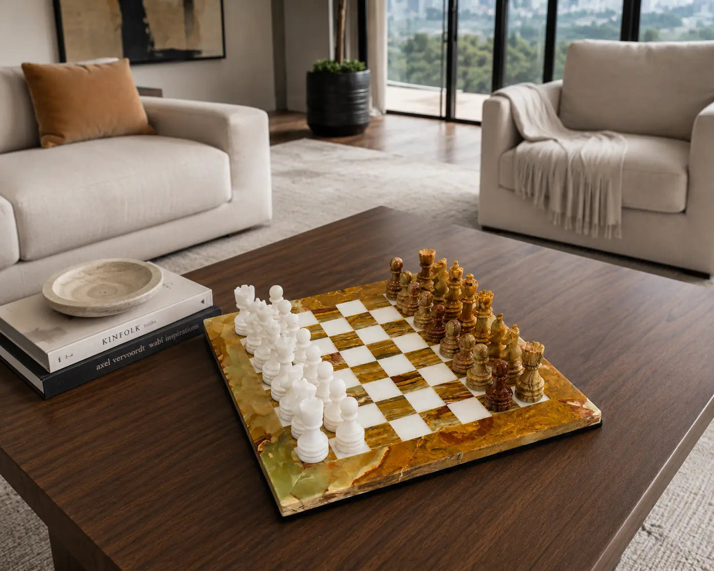 A luxury marble chessboard set on a dark wood coffee table in a modern living room. The chessboard features a polished gold and white marbled surface with white and dark brown chess pieces arranged for play.