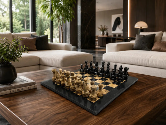 A luxury chess set with gold and black pieces on a dark wood and black board, styled on a wooden coffee table in a modern living room with beige sofas and large windows.