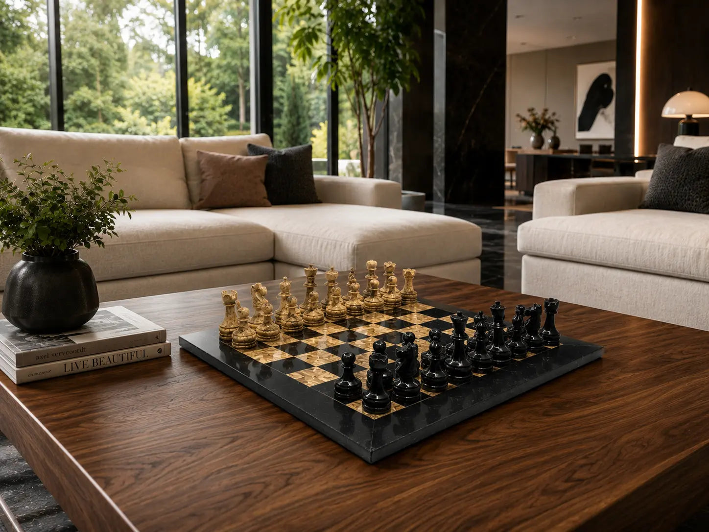 A black and gold chessboard with black chess pieces sits on a dark wood coffee table in a modern living room setting with beige sofas and large windows.
