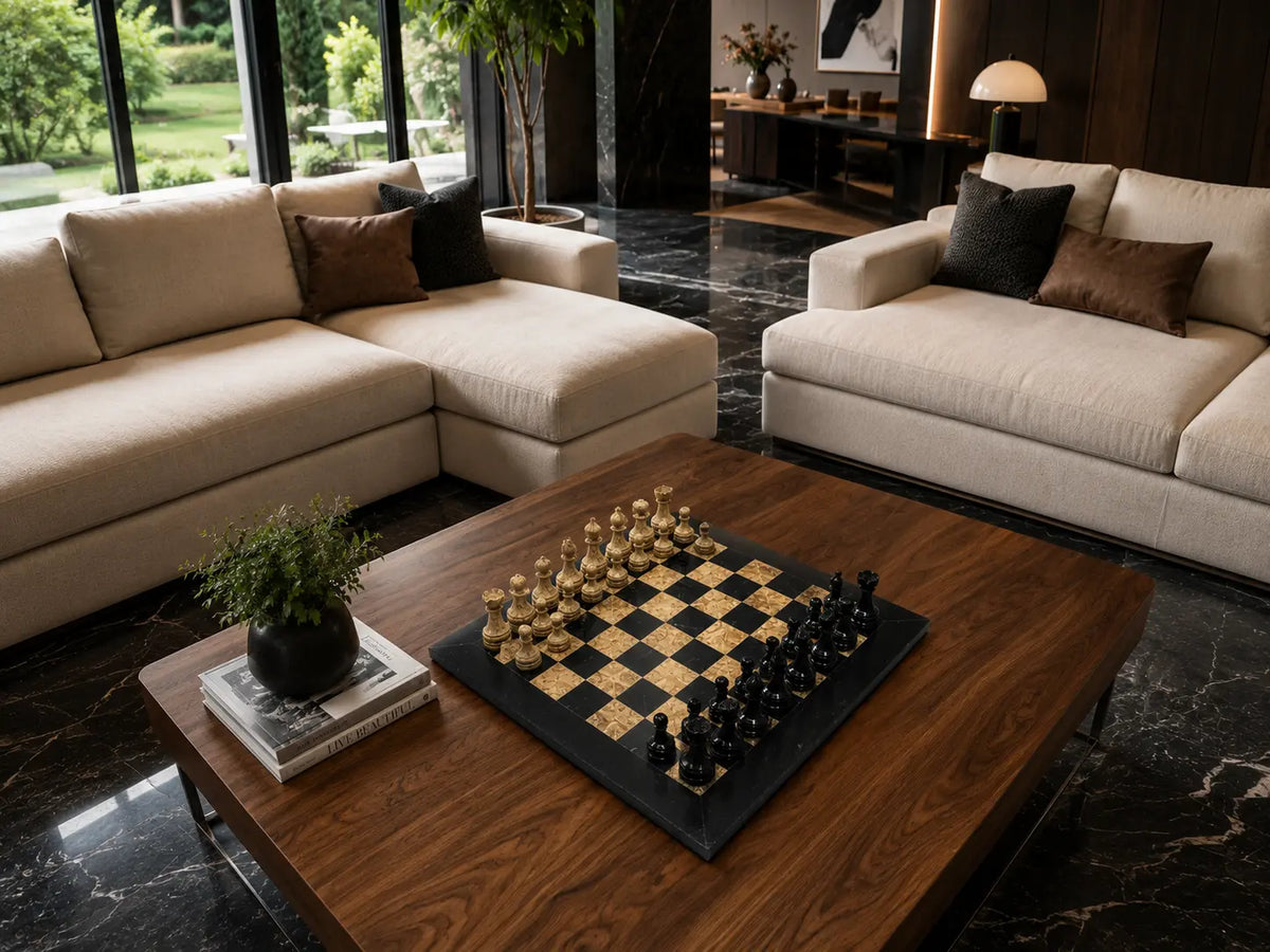 A modern living room scene with two cream sectional sofas, a dark wood coffee table holding a chessboard with gold and black chess pieces, black marble flooring, and large windows in the background.
