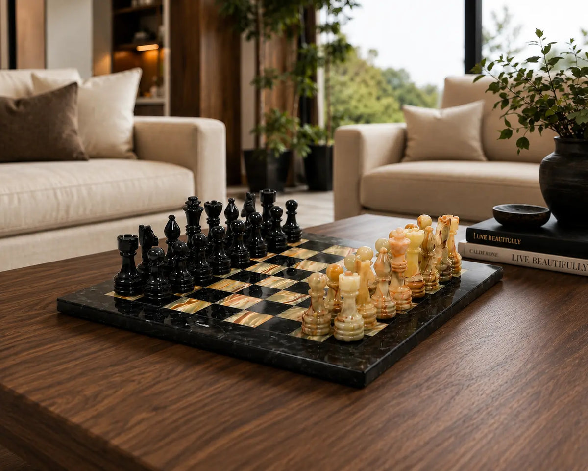A luxury chess set with black and cream-colored carved chess pieces on a black and gold checkered board, styled on a dark wood coffee table in a modern living room setting.