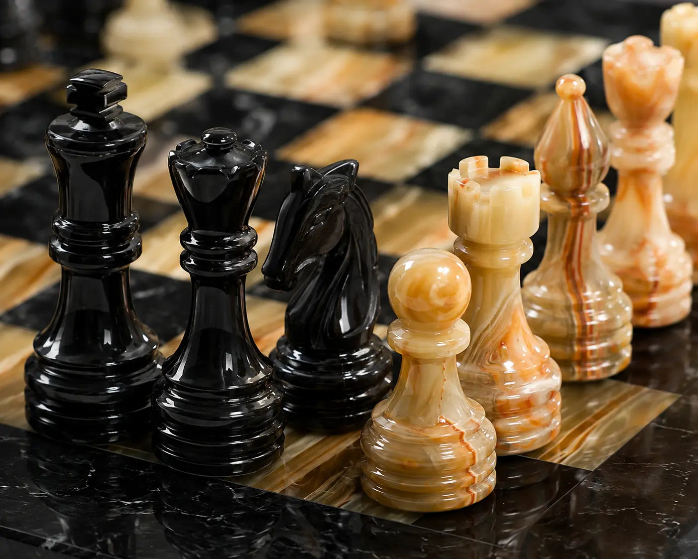 A close-up of a polished stone chess set on a matching marble chessboard, featuring glossy black pieces and cream and tan marbled pieces.