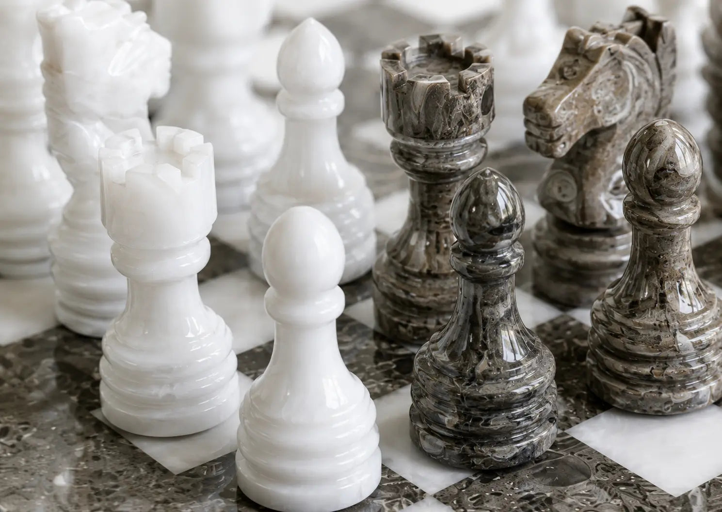 Close-up of polished marble chess pieces on a marble chessboard, including white pawns and dark gray rooks and horse pieces.