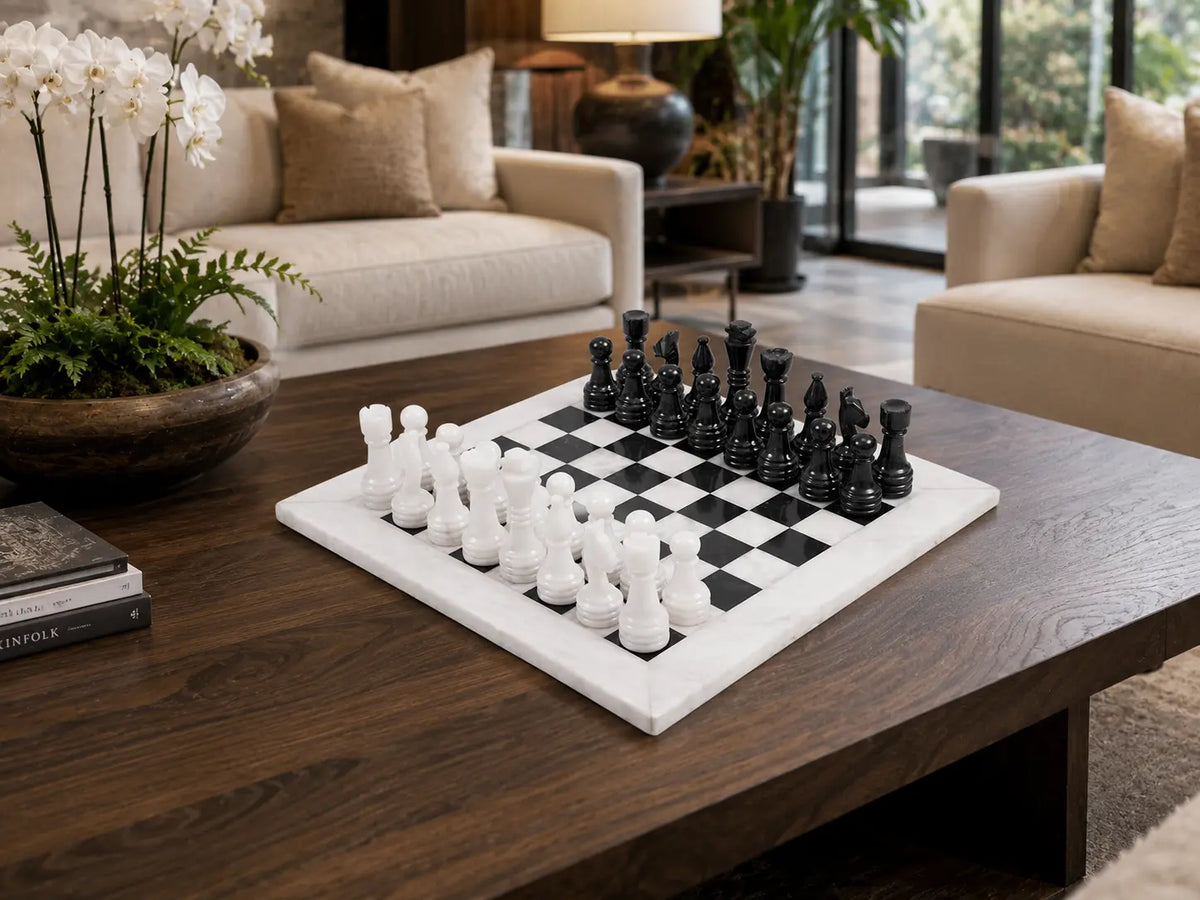 A square black-and-white checkered chessboard with matching chess pieces on a dark wood coffee table in a modern living room setting.