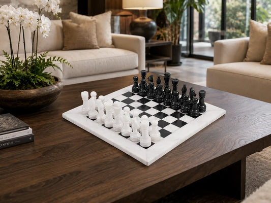 A square black-and-white checkered chessboard with matching chess pieces on a dark wood coffee table in a modern living room setting.