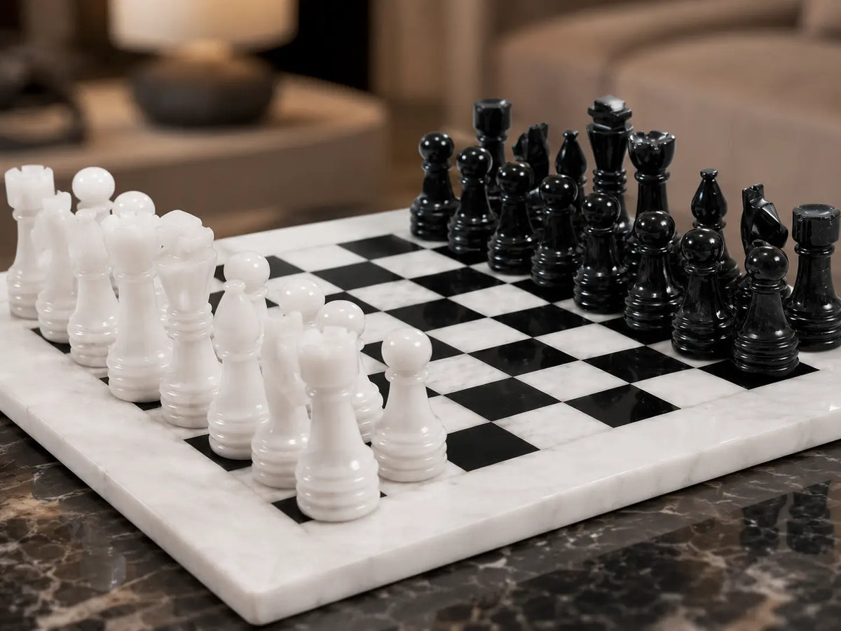 A marble chessboard with black and white checkered squares, holding white and black chess pieces, photographed on a dark marble tabletop with a softly blurred indoor background.