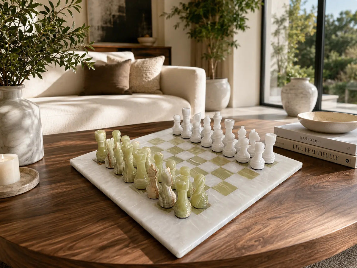 A marble chessboard with white and pale green chess pieces arranged on a round wooden coffee table in a bright, modern living room.