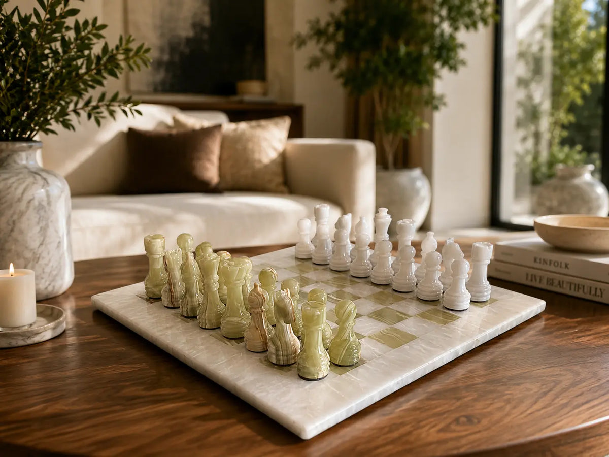 A marble chessboard with ivory and pale green chess pieces arranged on a wooden table in a styled living room setting.