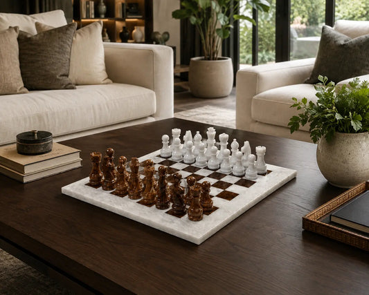 A marble chessboard with dark brown and white chess pieces set on a dark wood coffee table in a modern living room with beige sofas and potted plants.